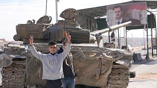 Opposition fighters stand next a government forces tank which was left on a highway, in Damascus, 8 December 2024
